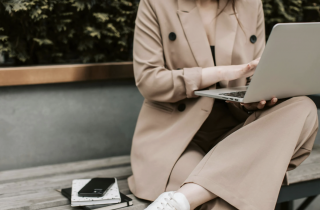 Woman in Tan Business Suit Sitting on a Bench with Laptop in Her Lap